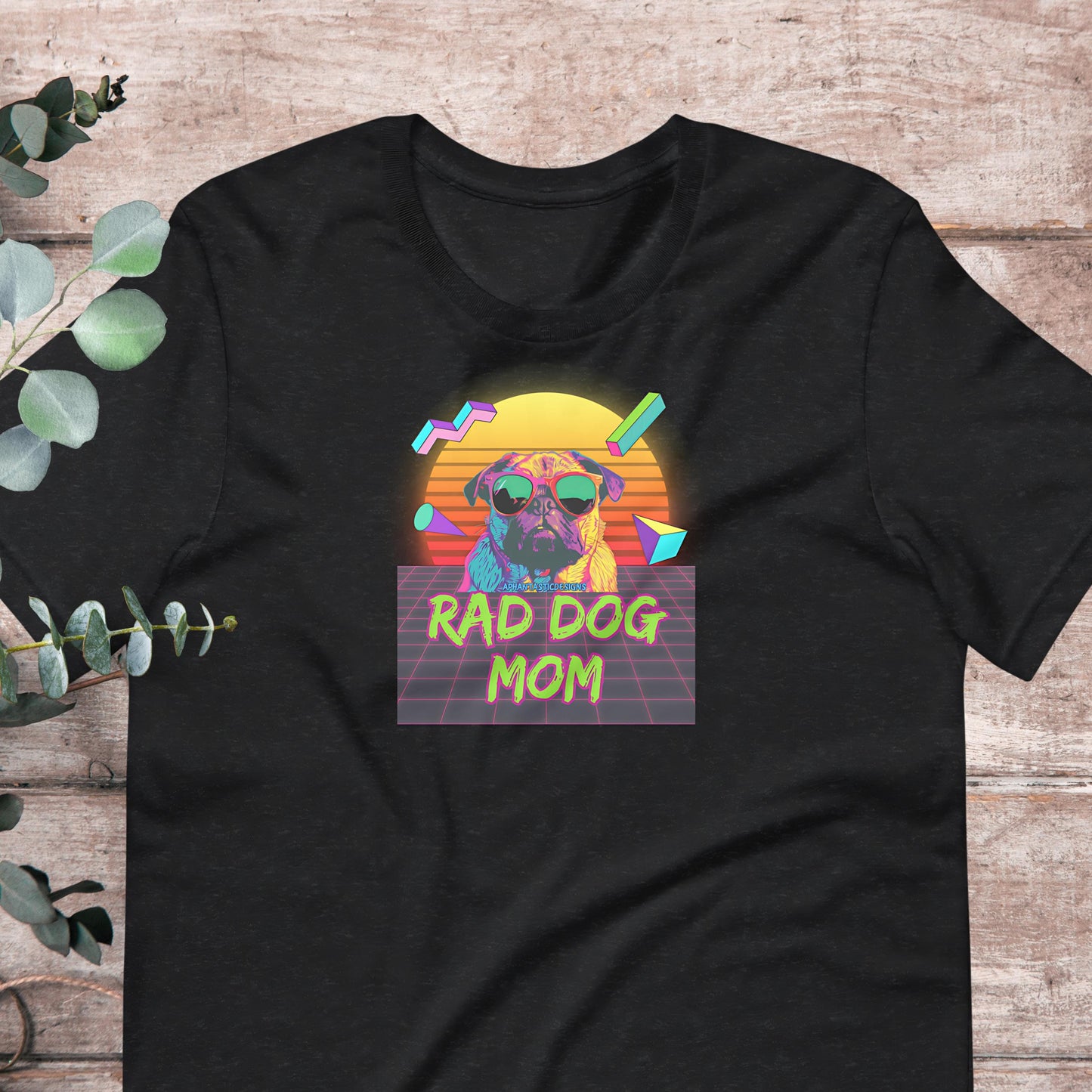 A black t-shirt with a graphic design featuring a pug dog wearing sunglasses and the text "RAD DOG MOM" against a colorful, retro-style background.