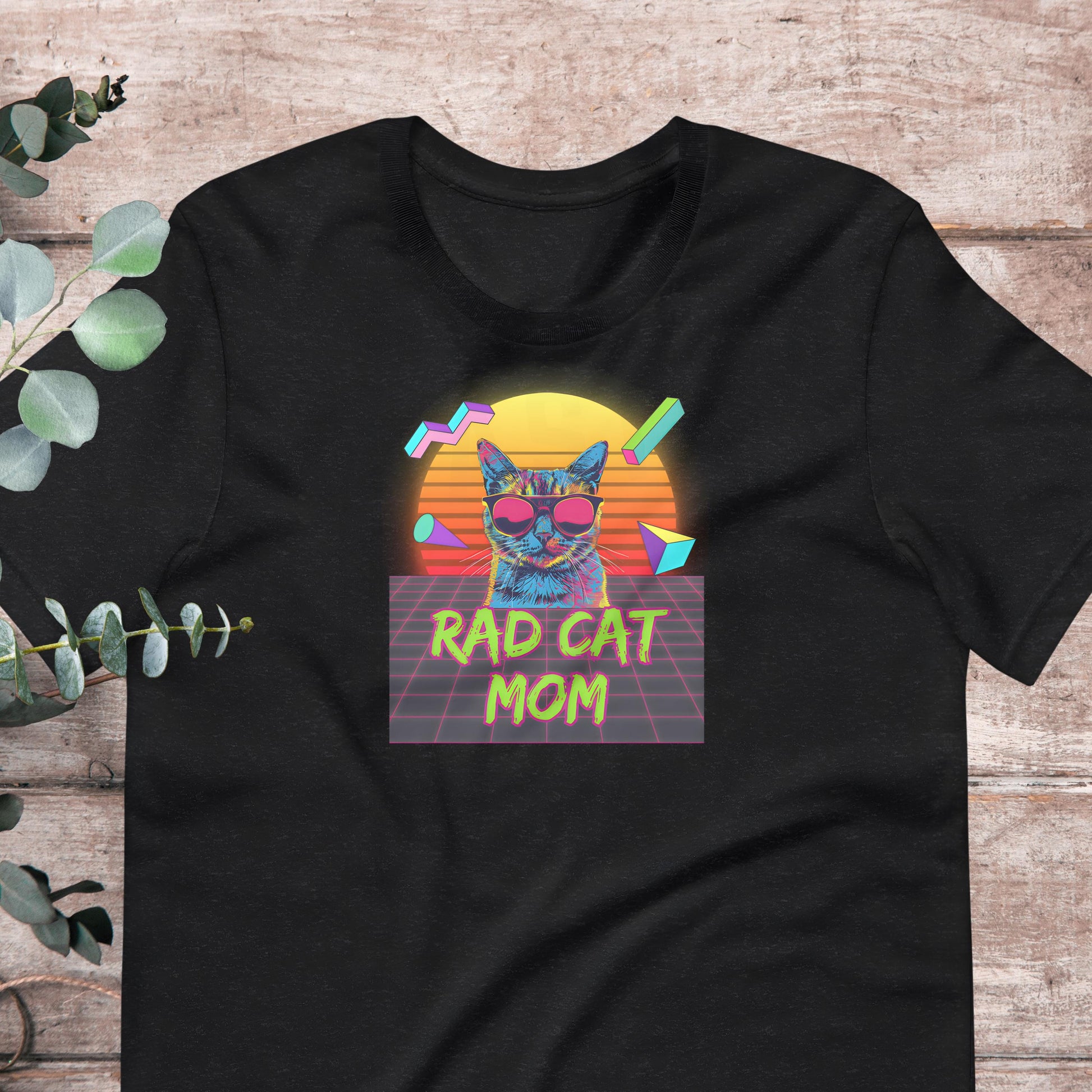 A black t-shirt with a graphic design featuring a cat wearing sunglasses and the text "RAD CAT MOM" against a colorful, retro-style background.
