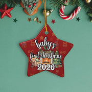 A red star-shaped ornament with the text "baby's first christmas 2026" is displayed against a green background, surrounded by Christmas decorations such as a star, candy cane, and pine branches.