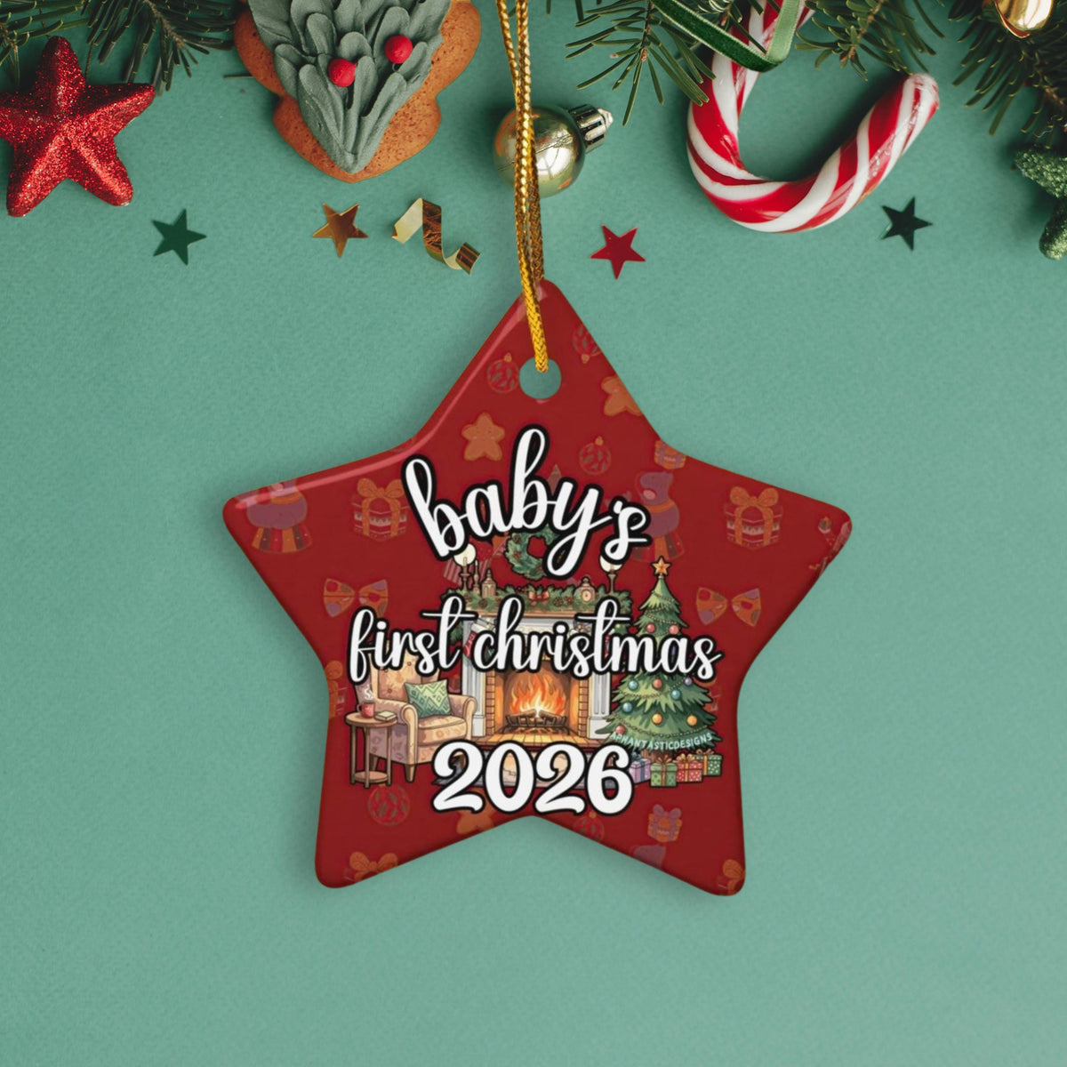 A red star-shaped ornament with the text "baby's first christmas 2026" is displayed against a green background, surrounded by Christmas decorations such as a star, candy cane, and pine branches.