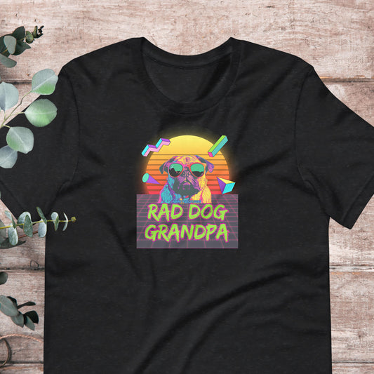 A black t-shirt with a graphic design featuring a pug dog wearing sunglasses and the text "RAD DOG GRANDPA" against a colorful sunset background.