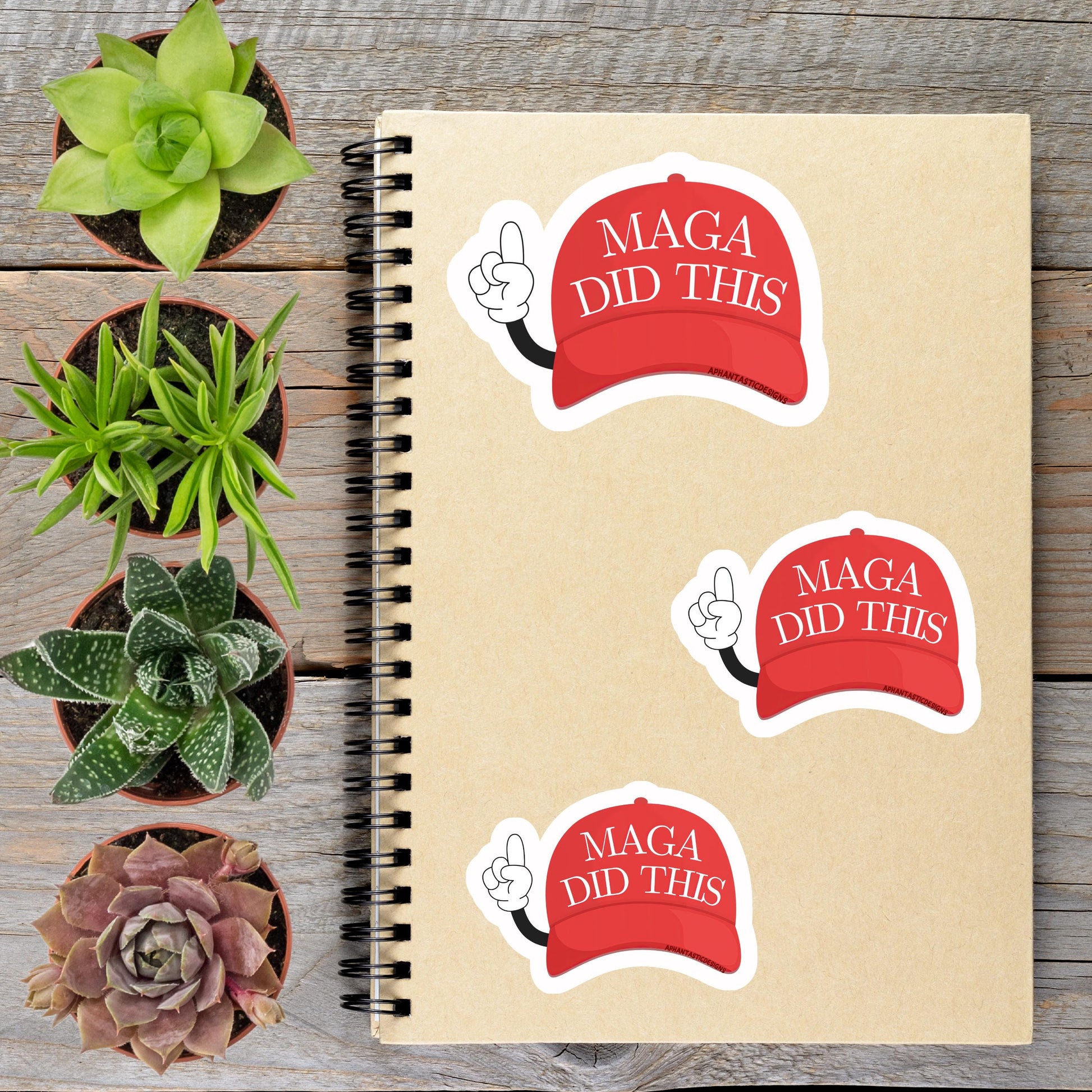 a spiral notebook with stickers on it, along with several potted plants arranged on a wooden surface.