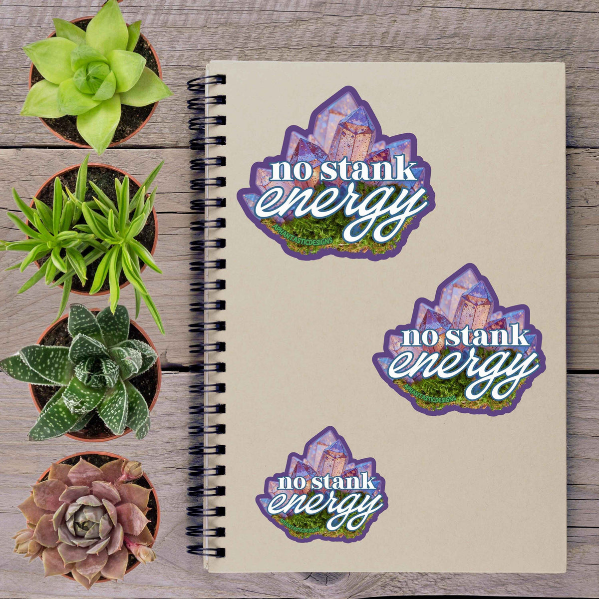 a notebook with stickers on it, along with several potted plants arranged on a wooden surface.