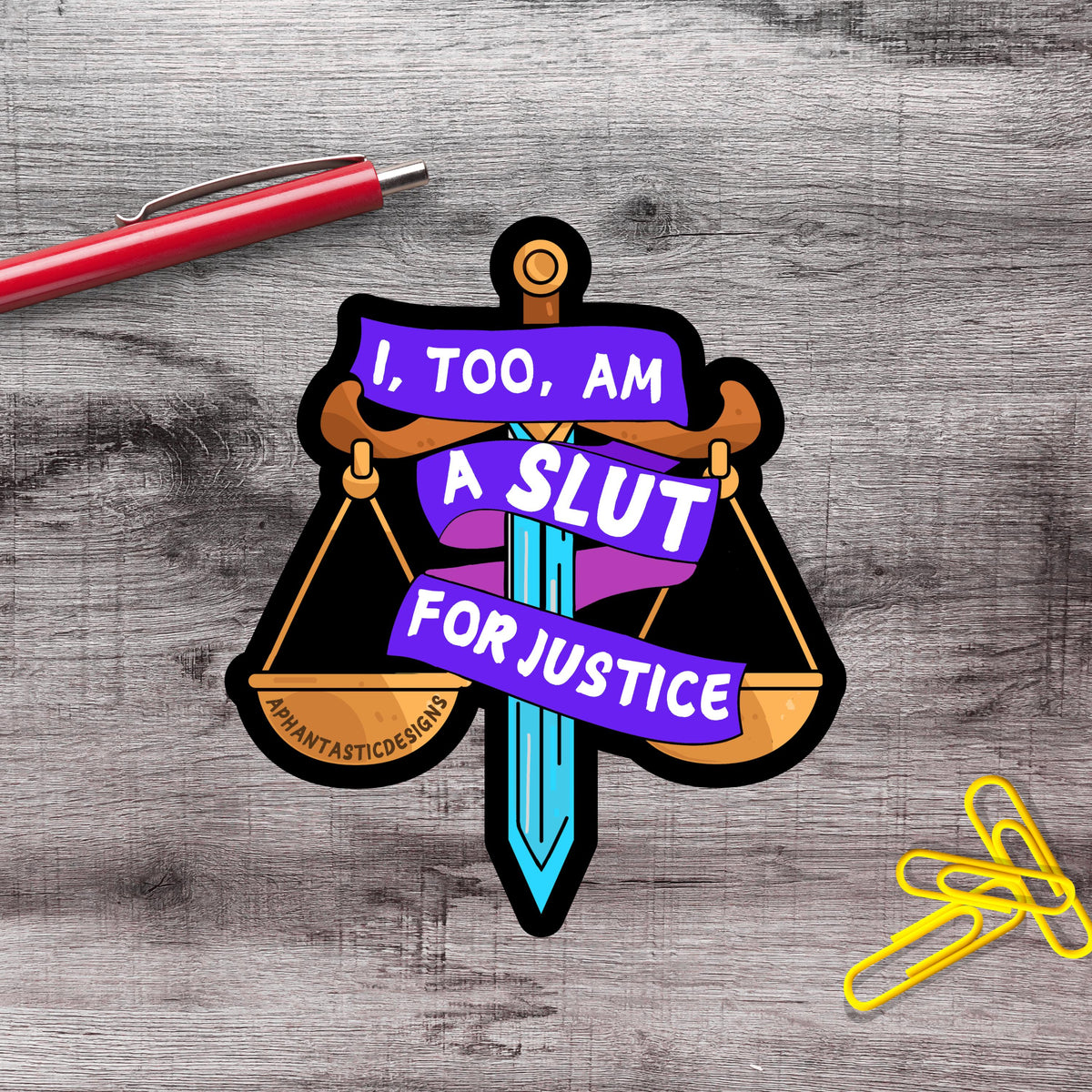 a sticker with a sword and scales, along with a red pen and yellow paper clips on a wooden surface.