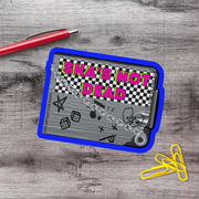 a sticker or decal with the text "Ska's not dead" on a blue and gray background, along with various graphic elements such as a checkerboard pattern, stars, and a broken heart. There is also a red pen and a few yellow paper clips on a wooden surface.