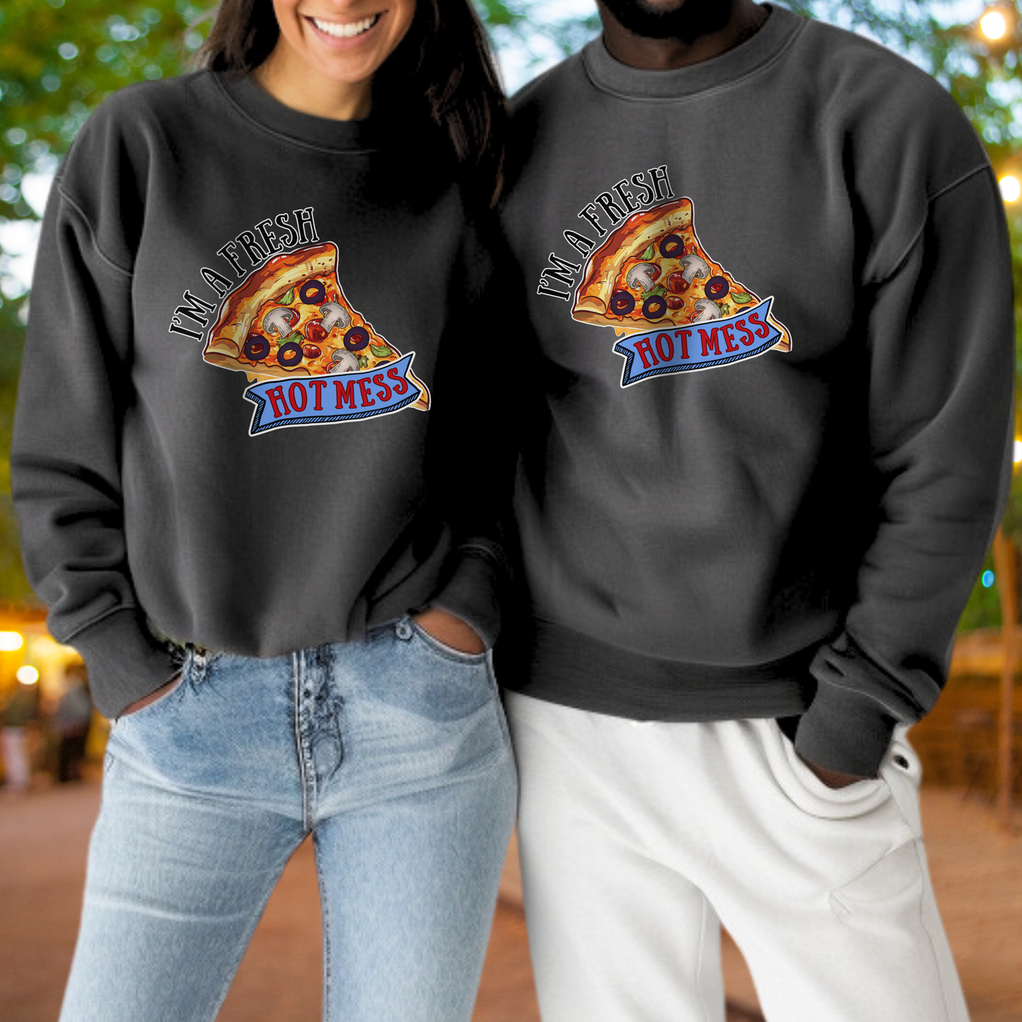 A woman and a man are standing next to each other, both wearing black sweatshirts with a pizza graphic and the text "I'm a fresh hot mess" printed on them.
