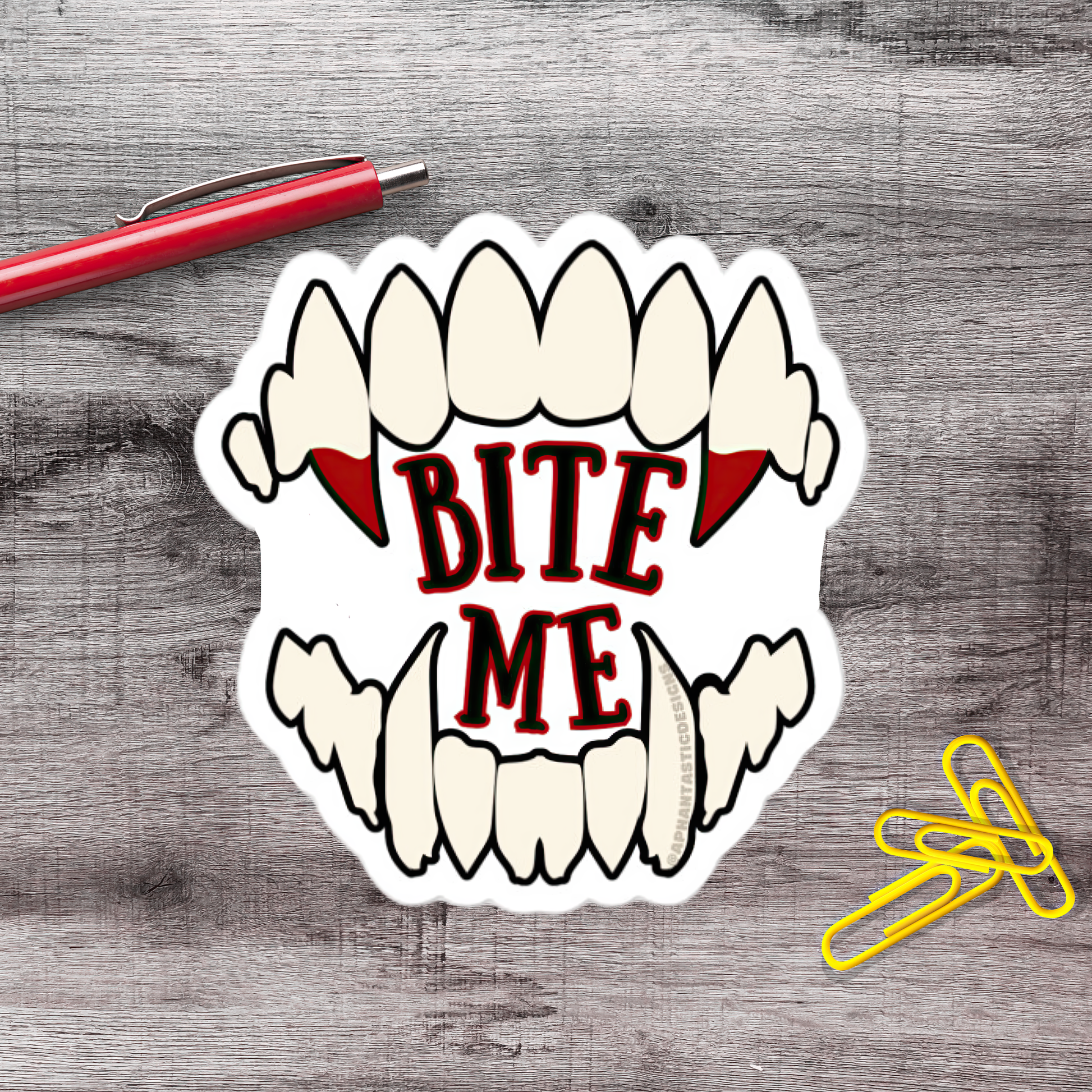 a sticker with a bite-out-of-the-mouth design and the text "BITE ME" on a wooden surface.