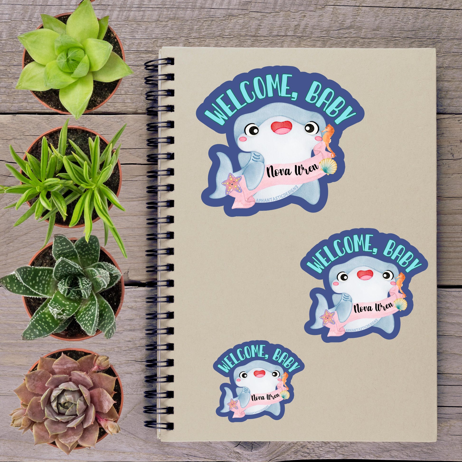 a spiral notebook with a welcome message sticker on the cover, surrounded by various potted plants and succulents.