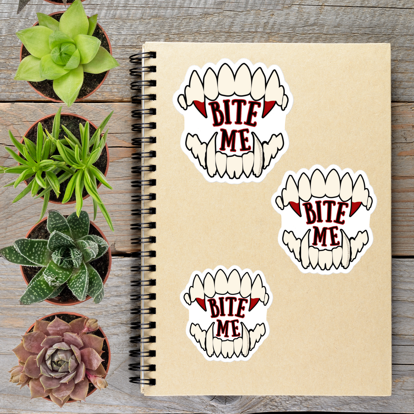 a spiral notebook with stickers on it, along with several potted plants arranged on a wooden surface.