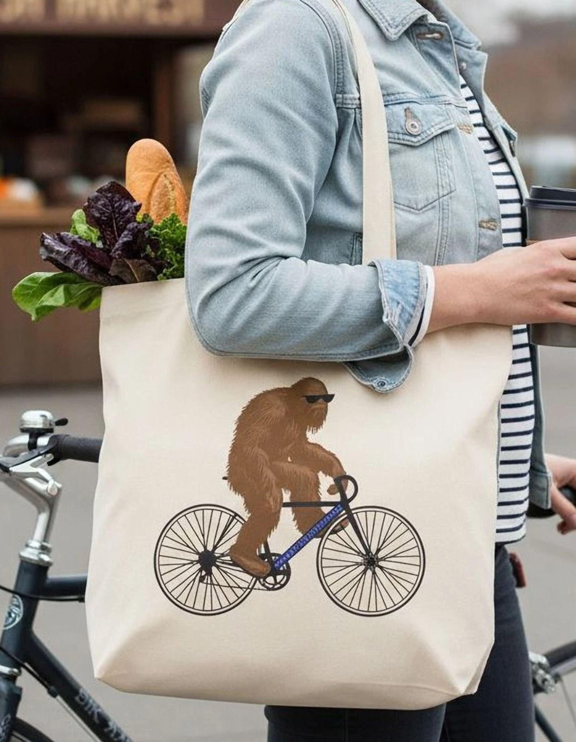 A woman is walking with a bicycle and carrying a bag with a cartoon image of a bear riding a bicycle.