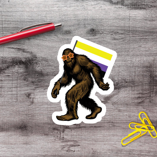 a sticker of a brown, furry creature with a yellow stripe on its back, standing on a wooden surface next to a red pen and a pile of yellow paper clips.
