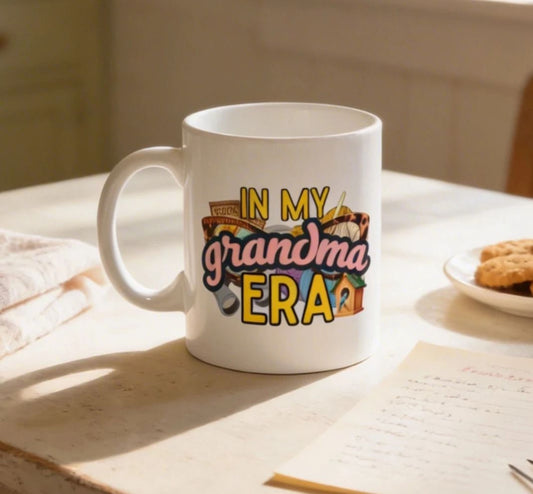 A white mug with a colorful design and text on it, placed on a table next to a plate of cookies and a piece of paper.