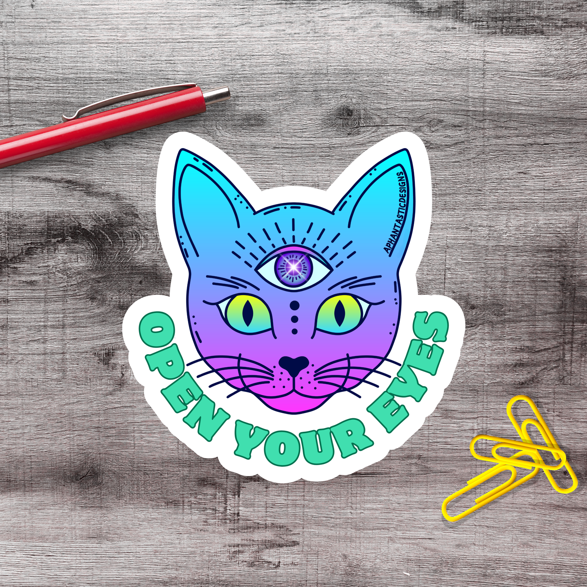A sticker featuring a colorful cat with an eye design, accompanied by the text "OPEN YOUR EYES" on a wooden surface.