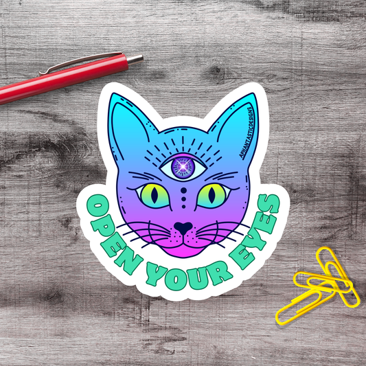 A sticker featuring a colorful cat with an eye design, accompanied by the text "OPEN YOUR EYES" on a wooden surface.