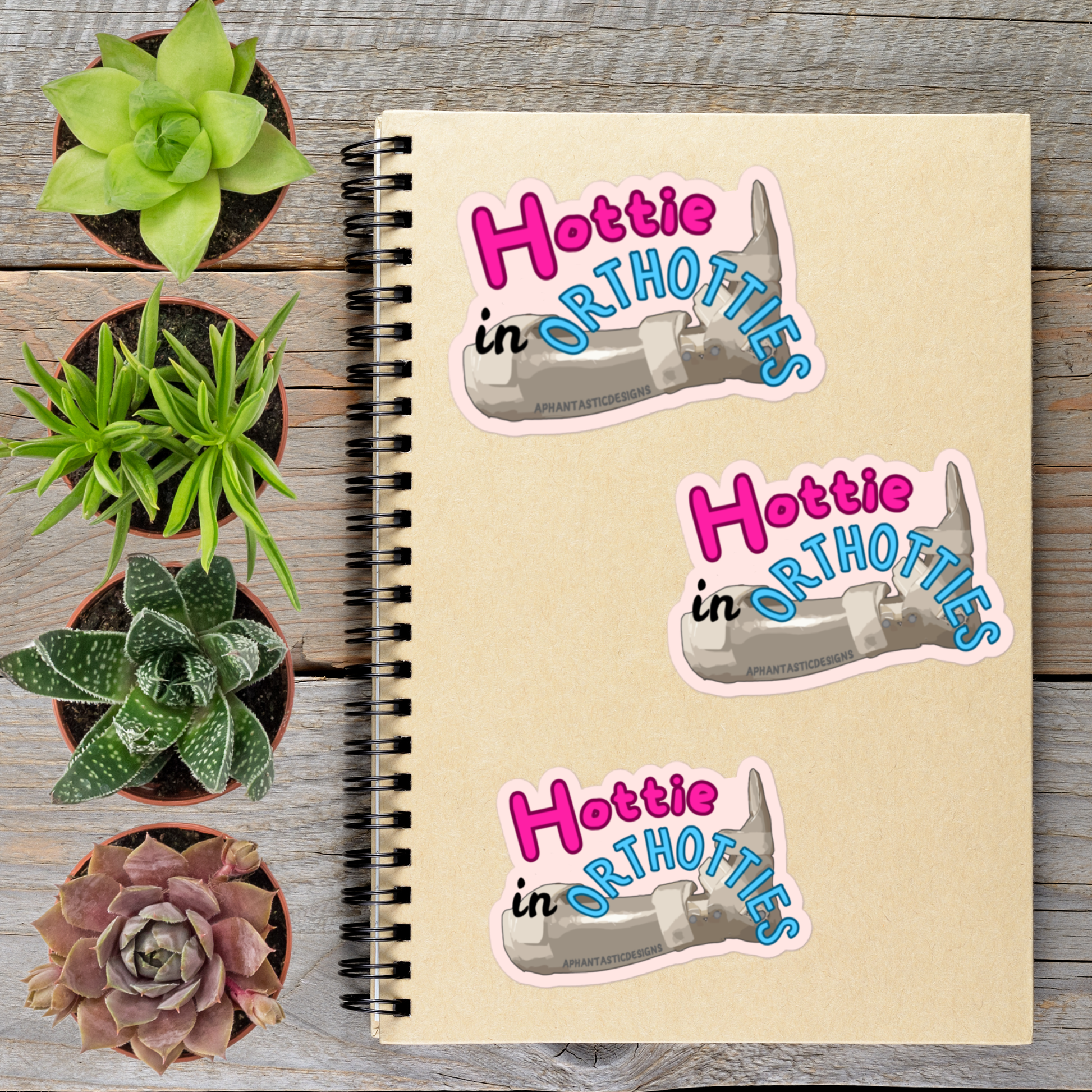 a notebook with stickers on it, surrounded by potted plants on a wooden surface.