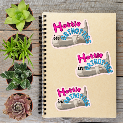 a notebook with stickers on it, surrounded by potted plants on a wooden surface.