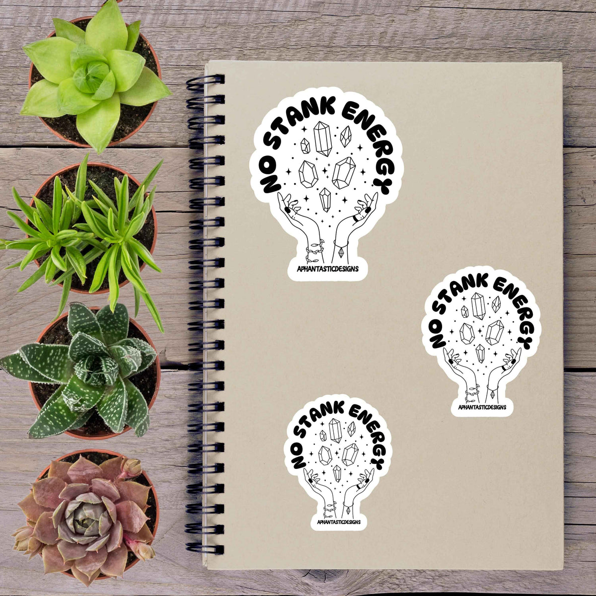a notebook with stickers on it, along with several potted plants arranged on a wooden surface.