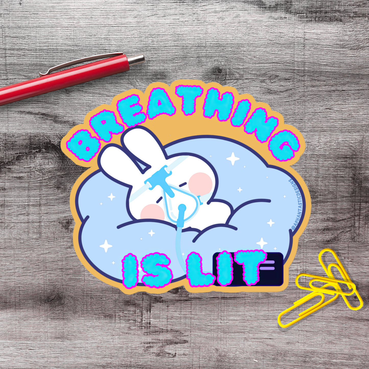 A sticker with a cartoon rabbit and the text "BREATHING IS LIT" on a wooden surface.