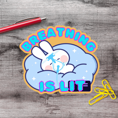 A sticker with a cartoon rabbit and the text "BREATHING IS LIT" on a wooden surface.