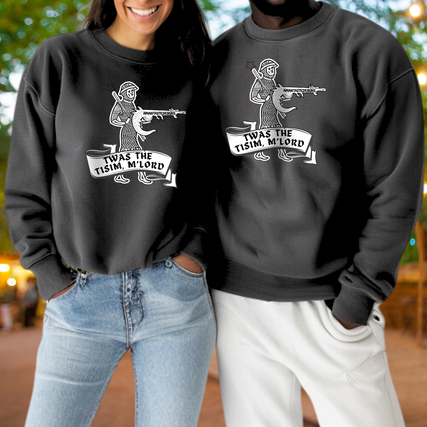 A woman and a man standing together, both wearing black sweatshirts with a graphic design featuring a figure holding a gun and the text "TWAS THE TISIM M LORD".