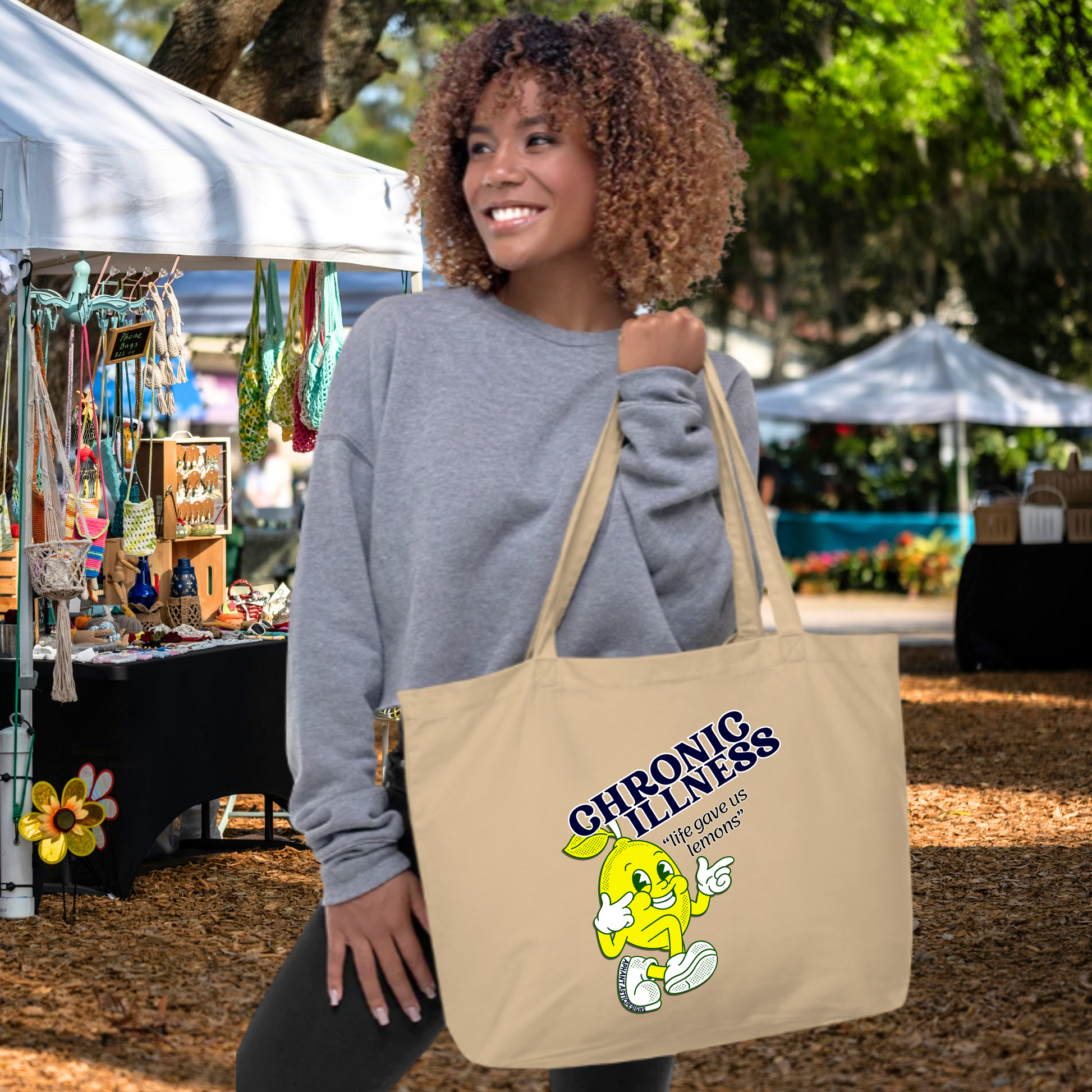 A woman with curly hair is standing in front of a tent, holding a large tote bag with a cartoon character on it.