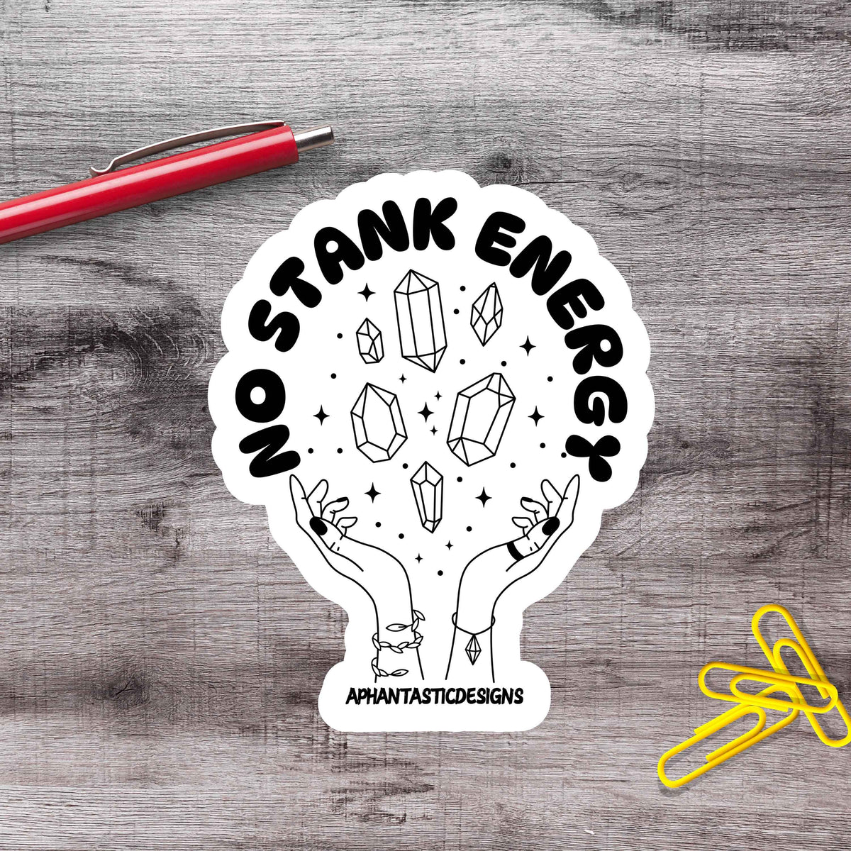 A sticker with a hand holding a crystal surrounded by stars, with the text "No Stank Energy" and "Aphantastic Designs" written on it.