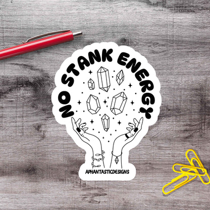 A sticker with a hand holding a crystal surrounded by stars, with the text "No Stank Energy" and "Aphantastic Designs" written on it.
