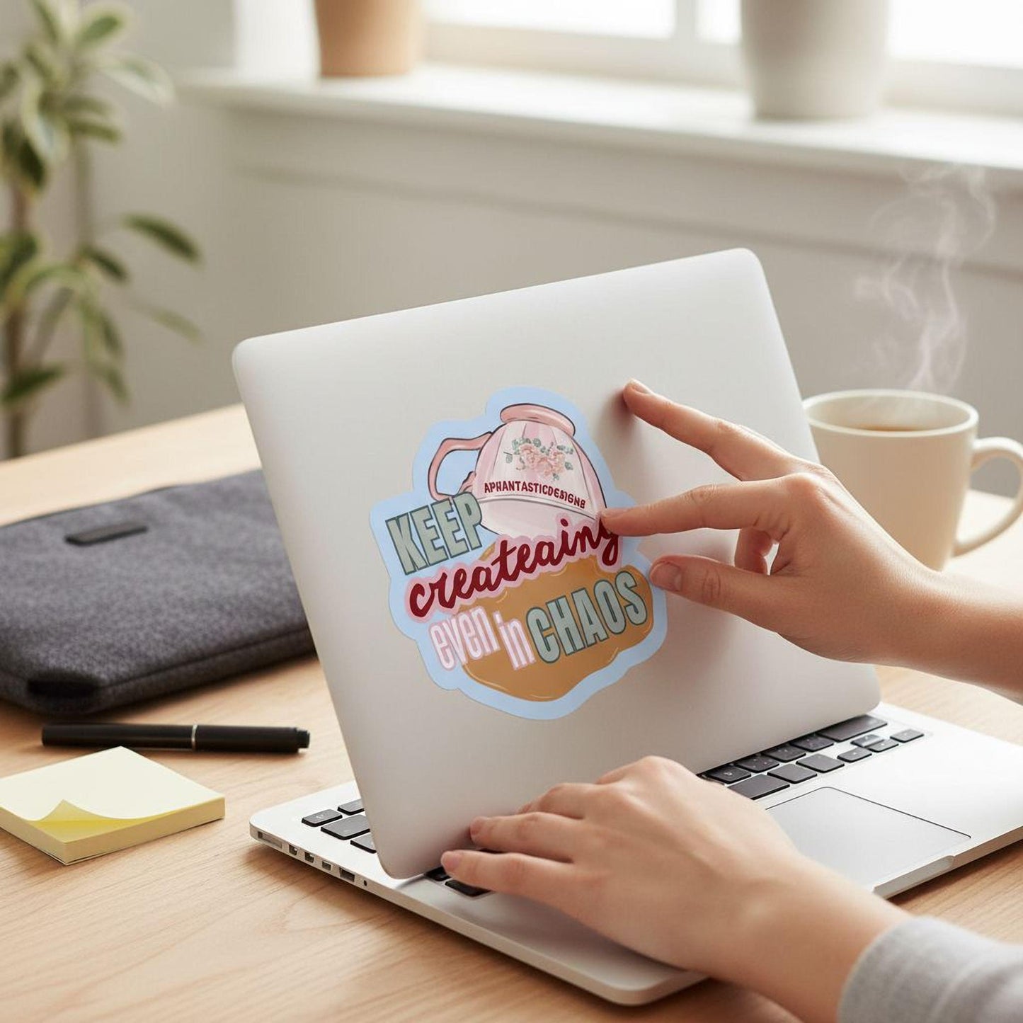 A person's hands are shown typing on a laptop with a sticker on the lid that says "KEEP CREATING EVEN IN CHAOS".