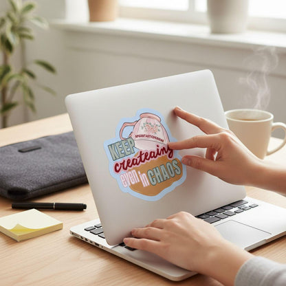 A person's hands are shown typing on a laptop with a sticker on the lid that says "KEEP CREATING EVEN IN CHAOS".