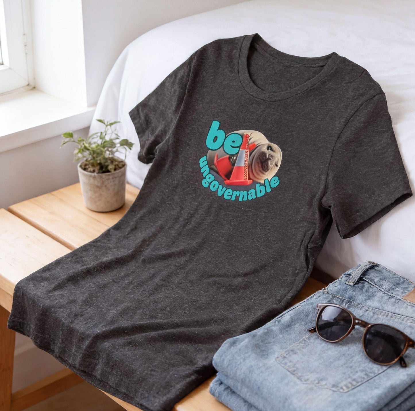 a casual outfit laid out on a wooden bench, including a gray t-shirt with a graphic, a pair of jeans, and a pair of sunglasses.