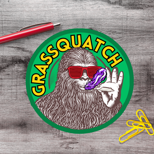 a circular sticker with a cartoon-like depiction of a furry creature wearing sunglasses and holding a purple object, with the text "GRASSQUATCH" written around the edge.