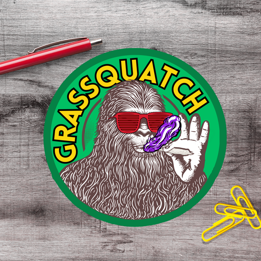 a circular sticker with a cartoon-like depiction of a furry creature wearing sunglasses and holding a purple object, with the text "GRASSQUATCH" written around the edge.