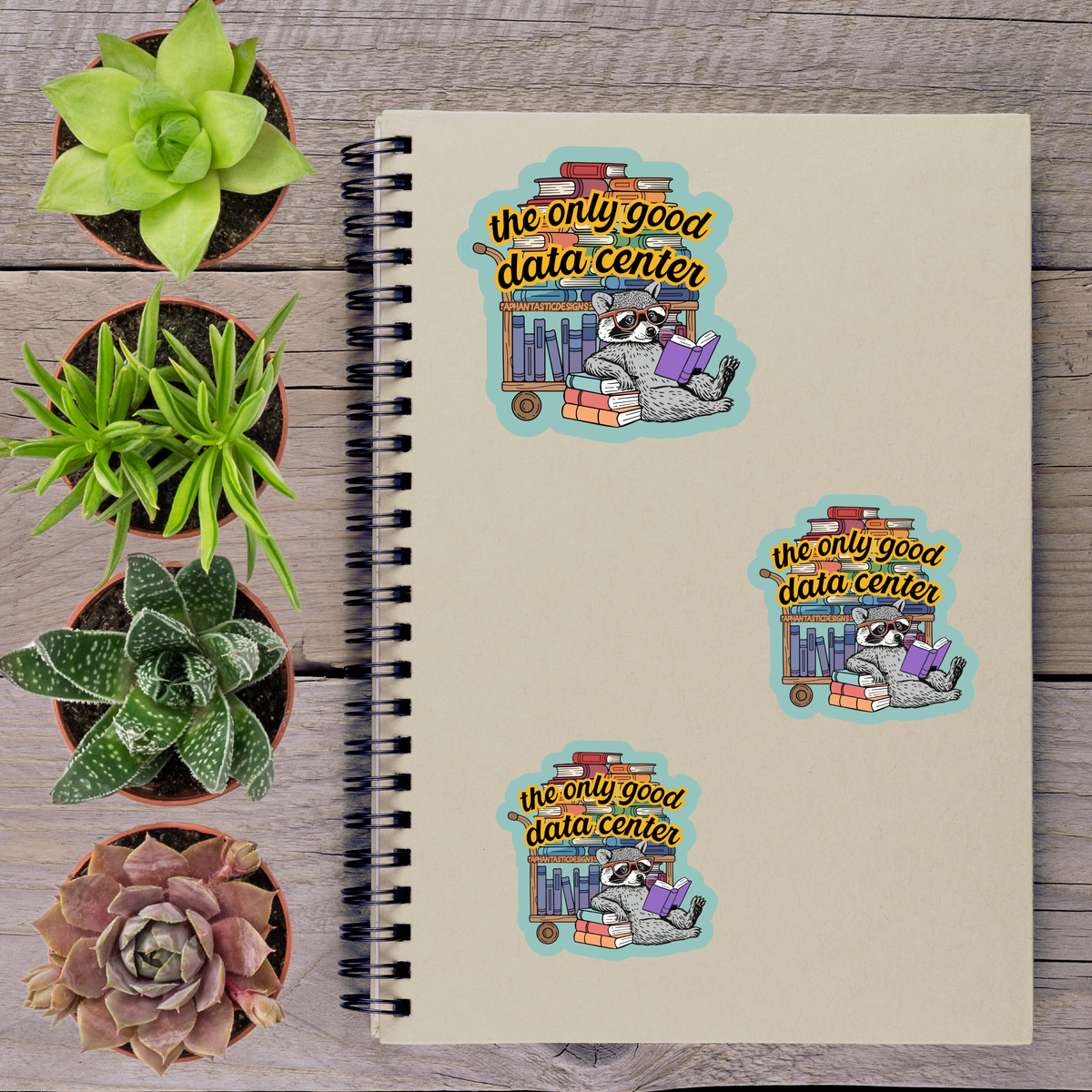 a spiral notebook with stickers on it, along with several potted plants arranged on a wooden surface.