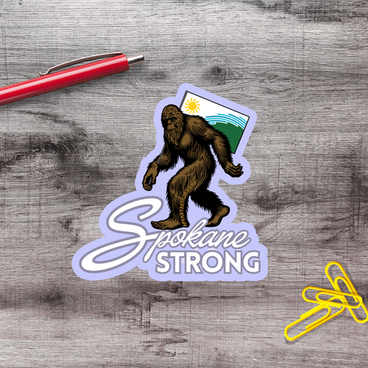 a sticker with a cartoon depiction of a large, furry creature, likely a Sasquatch, and the text "Spokane Strong" written below it.