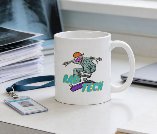 A white coffee mug with a graphic design featuring a skateboarder and the text "RAD TECH" on it, placed on a desk with a laptop and some papers.