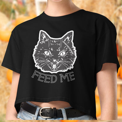 A person wearing a black crop top with a white graphic of a cat and the text "FEED ME" printed on it.