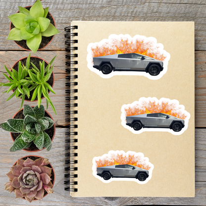 a spiral notebook with three stickers on it, depicting a silver truck with flames on top. The stickers are arranged in a row on the notebook, with the largest sticker on the left, the middle sticker slightly smaller, and the smallest sticker on the right. The notebook is placed on a wooden surface, with several potted plants surrounding it.