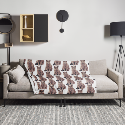 a cozy living room with a gray sofa adorned with a blanket that has a repeating pattern of brown cats. The room is decorated with a wooden cabinet, a clock, and a lamp, creating a warm and inviting atmosphere.
