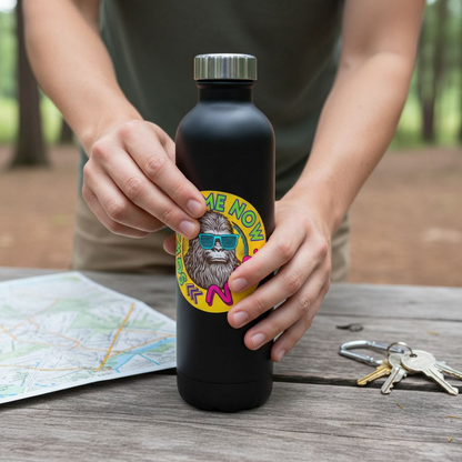 A person is holding a black water bottle with a sticker featuring a cartoon character, and there are keys and a map on a wooden surface in the background.