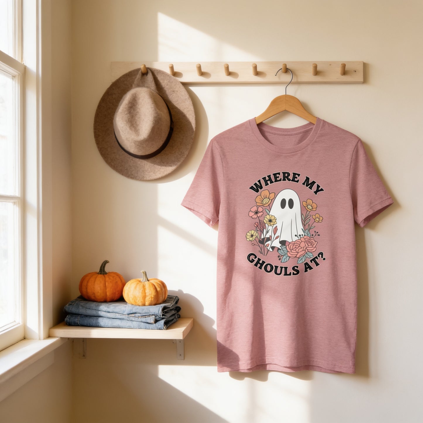 a pink t-shirt hanging on a wooden hanger, with a hat and two pumpkins placed on a shelf below it.