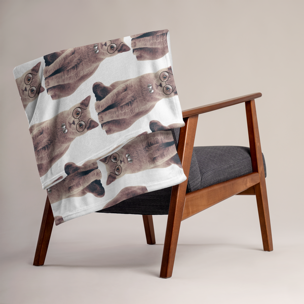 a chair with a blanket that has a repeating pattern of cats on it.