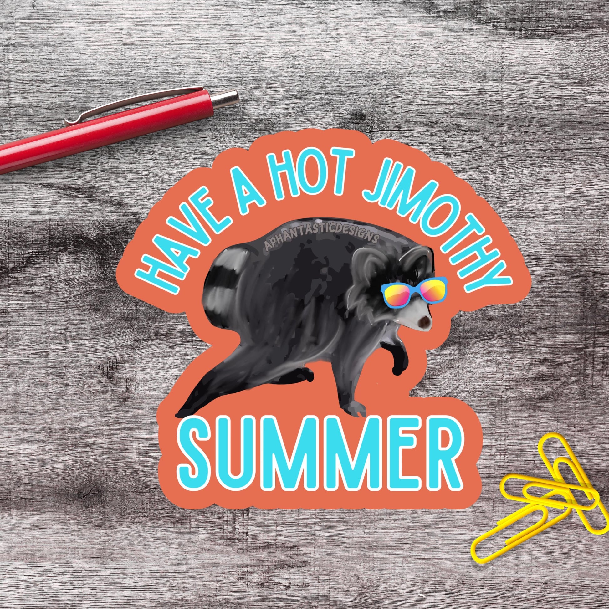 a sticker with a raccoon wearing sunglasses and the text "Have a hot jimothy summer" on a wooden surface.