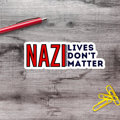 a sticker with the text "NAZI LIVES DON'T MATTER" on a wooden surface, along with a red pen and yellow paper clips.