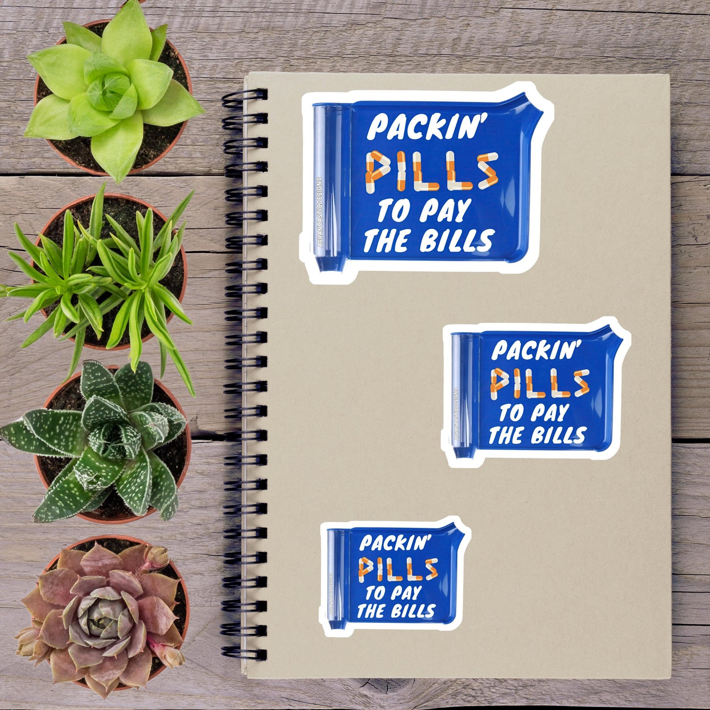 a spiral notebook with three stickers on it, along with four potted plants arranged on a wooden surface.