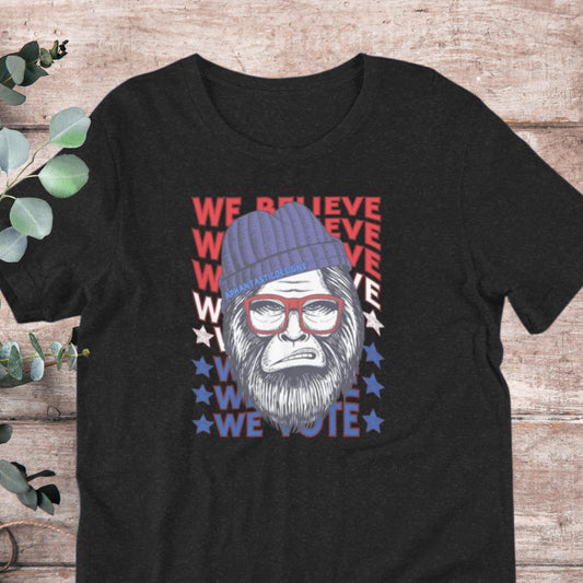 A black t-shirt with a graphic design featuring a cartoon-like gorilla wearing a blue beanie and glasses, along with the text "We Believe We Vote" in a patriotic style.