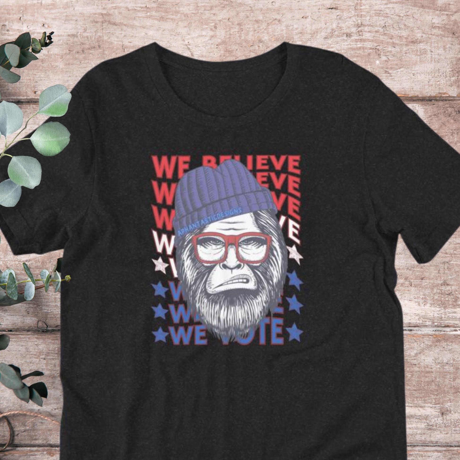 A black t-shirt with a graphic design featuring a cartoon-like gorilla wearing a blue beanie and glasses, along with the text "We Believe We Vote" in a patriotic style.