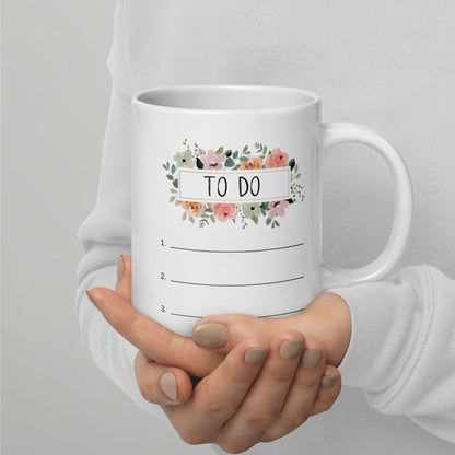 A person is holding a white mug with a floral design and the text "TO DO" written on it.