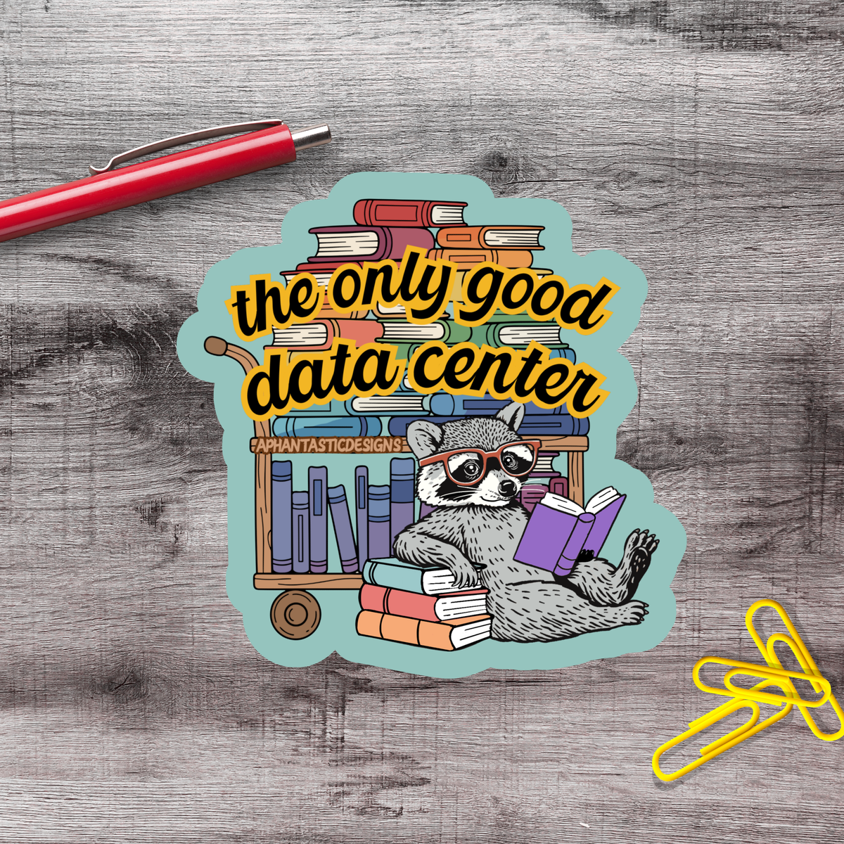 A sticker with a raccoon sitting on a bookshelf and reading a book, surrounded by various books.