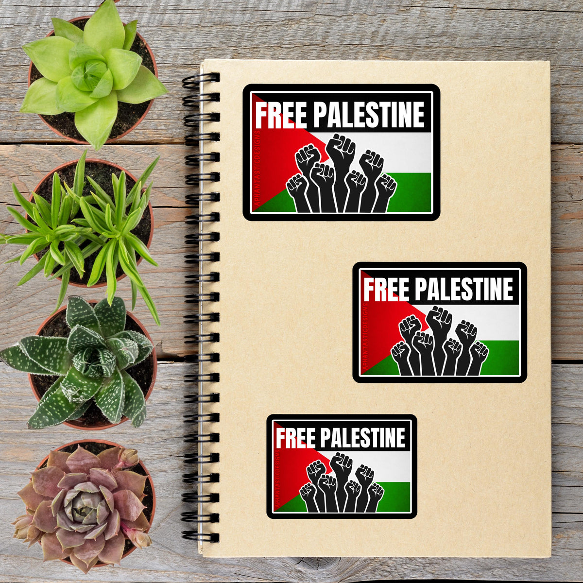 a notebook with three stickers on it, along with several potted plants arranged on a wooden surface.