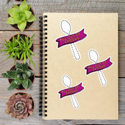 a notebook with stickers on it, surrounded by potted plants on a wooden surface.
